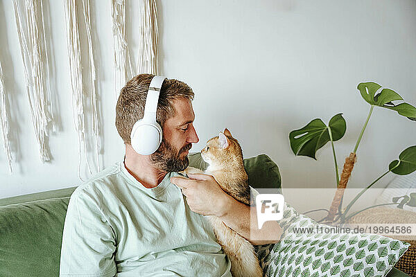 Man with cat wearing headphones and sitting on the couch at home