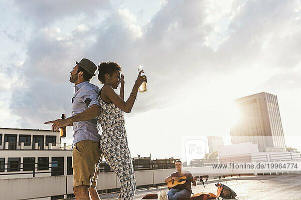 Man with woman holding beer and dancing on rooftop