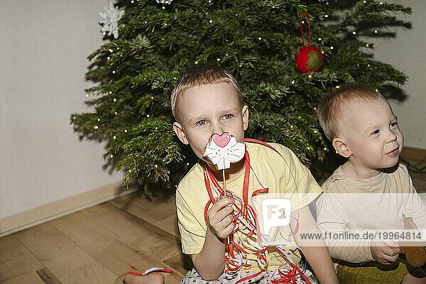 Boy holding Christmas cookie and sitting with brother at home