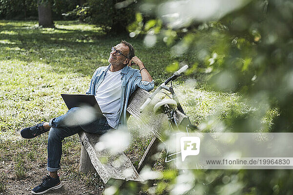 Thoughtful man with laptop sitting on bench in park