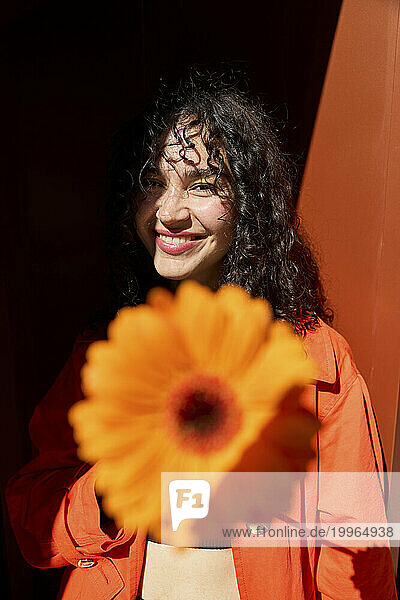 Smiling woman with gerbera flower in front of wall