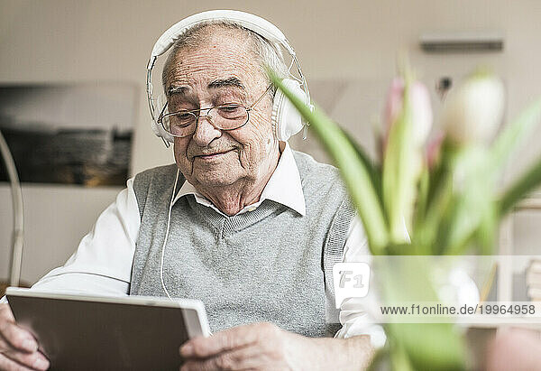 Smiling senior man wearing headphones and using tablet PC at home