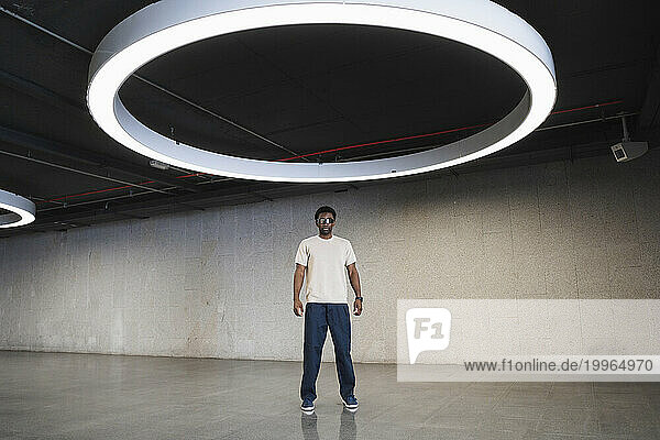 Young man with futuristic cyber glasses standing under modern ring lamp