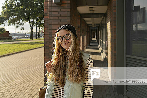 Smiling blond woman with eyeglasses standing on footpath