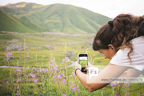 Young woman photographing flowering plants through smart phone