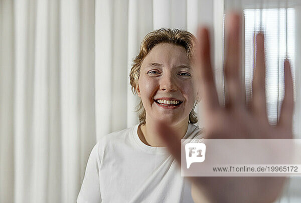 Happy woman showing stop gesture in front of white curtain