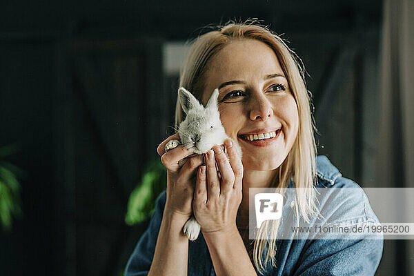Happy woman holding bunny near face at home