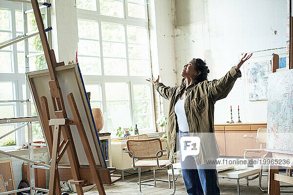 Smiling artist standing with arms outstretched in art studio
