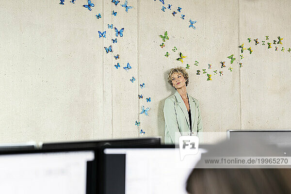 Businesswoman standing in front of wall with butterflies sticker on it at office
