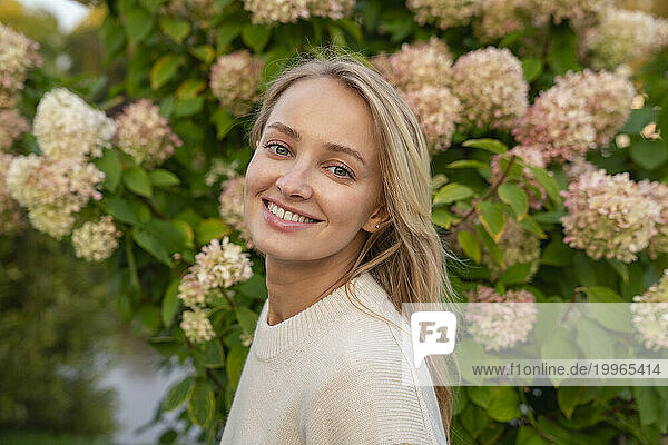 Happy blond woman in front of flowering plant