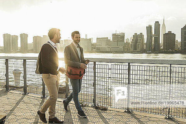 Happy young colleagues talking by river at sunset in New York City  USA