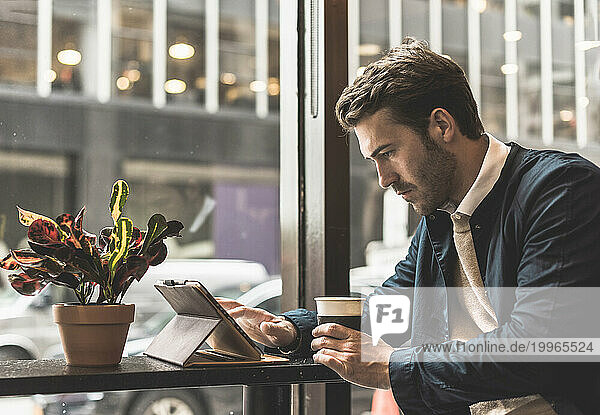 Young businessman holding disposable cup and using tablet PC at cafe