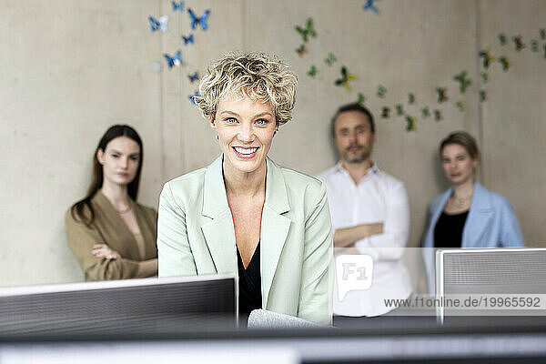 Smiling businesswoman with colleagues in background at workplace