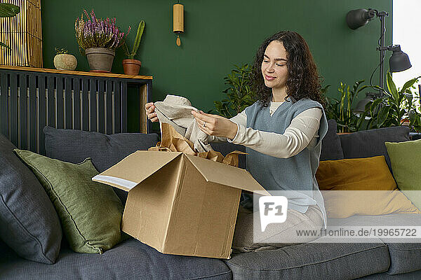 Woman looking at dress from box sitting on sofa at home