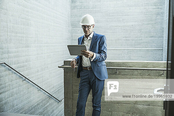 Senior engineer wearing hardhat and using tablet PC near wall
