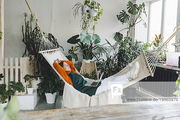 Botanist relaxing on hammock with laptop in plant store