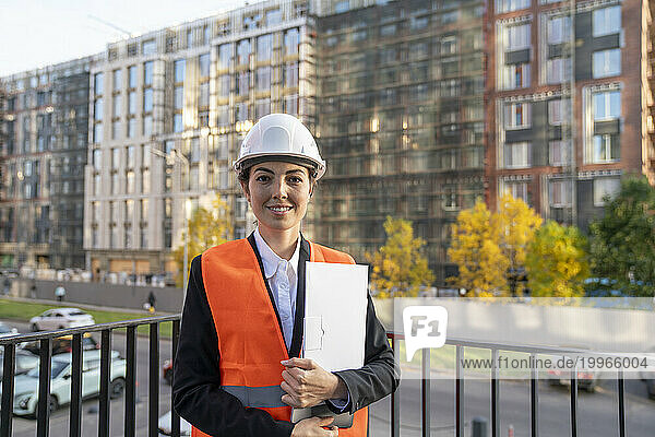 Smiling engineer holding file folder and standing in balcony