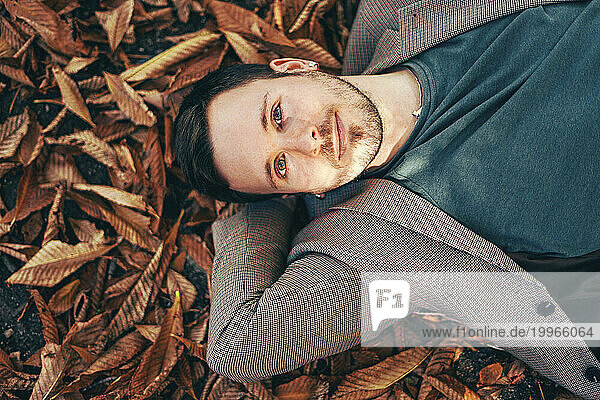 Smiling young man relaxing on autumn leaves