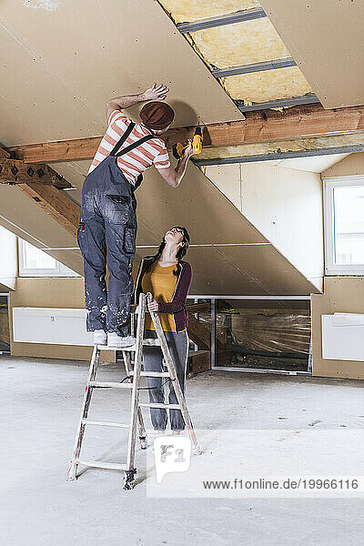 Man standing on ladder and drilling wall with woman at home