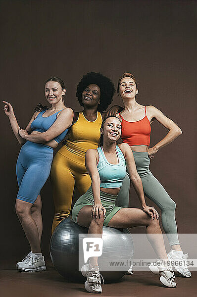 Smiling female friends with fitness ball against brown background