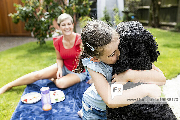 Girl embracing and kissing dog in back yard