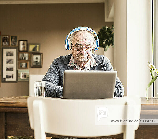 Senior man wearing headphones and using laptop at home