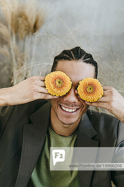 Smiling businessman covering eyes with Gerbera flowers in garden