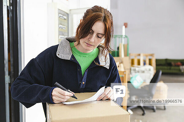 Delivery woman doing paperwork for package at distribution warehouse
