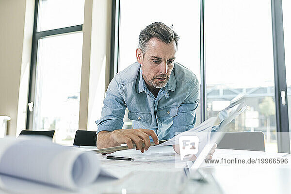 Architect leaning on desk and working with documents in office