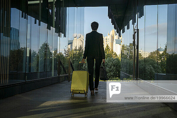 Businesswoman pulling suitcase amidst glass wall