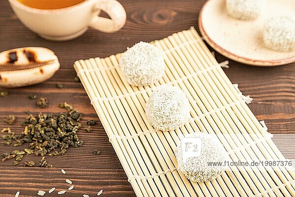 Japanischer Reis süße Brötchen Mochi gefüllt mit Pandan und Kokosnuss Marmelade und Tasse grüner Tee auf braunem Holz Hintergrund. Seitenansicht  Nahaufnahme  selektiver Fokus