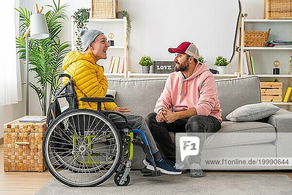 Behinderter Mann im Rollstuhl und Freunde unterhalten sich entspannt im Wohnzimmer des Hauses