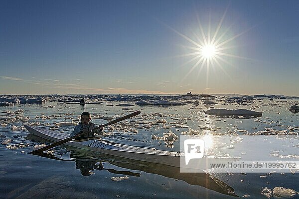 Kind paddelt in Seekayak durch Eisschollen im Meer  Kayak  Gegenlicht  Sonnenstrahlen  Sommer  Ilulissat  Diskobucht  Grönland  Nordamerika