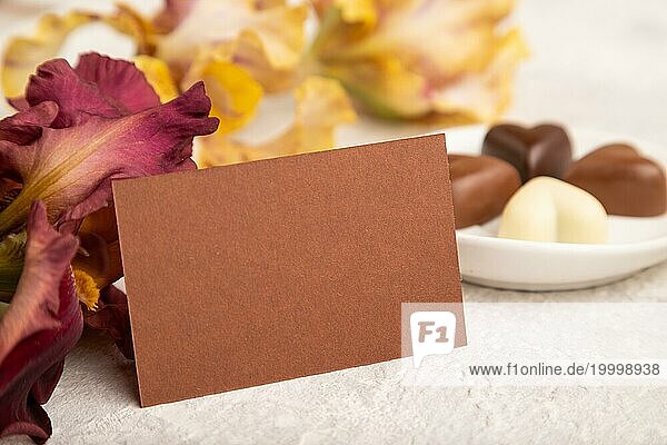 Braune Visitenkarte mit Schokoladenbonbons und Irisblüten auf grauem Betonhintergrund. Seitenansicht  Kopierraum  Stillleben. Frühstück  Morgen  Frühling Konzept