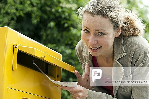 Young woman drops a letter in the letterbox