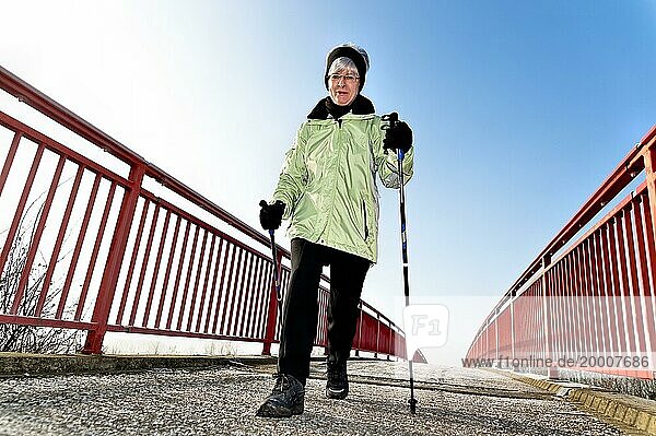 Frau läuft beim Nordic walking über eine Brücke mit rotem Geländer