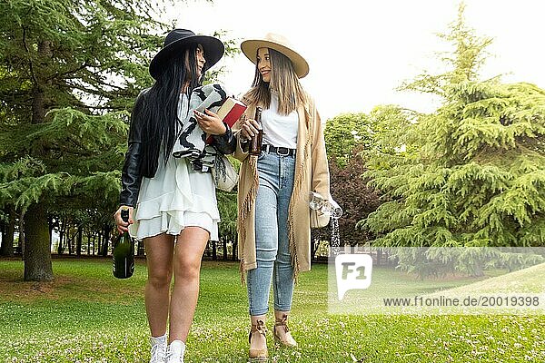 Vorderansicht eines lesbischen Paares  das mit einer Flasche Sekt und Gläsern im Park spazieren geht  um seine Verlobung zu feiern