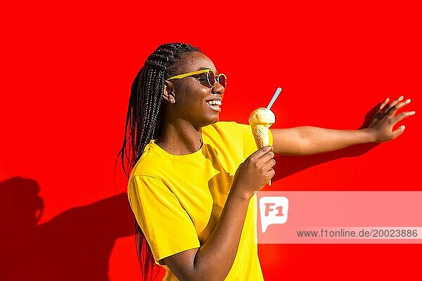 Glückliche junge afrikanische Frau isst ein Eis und lehnt sich an eine rote Wand