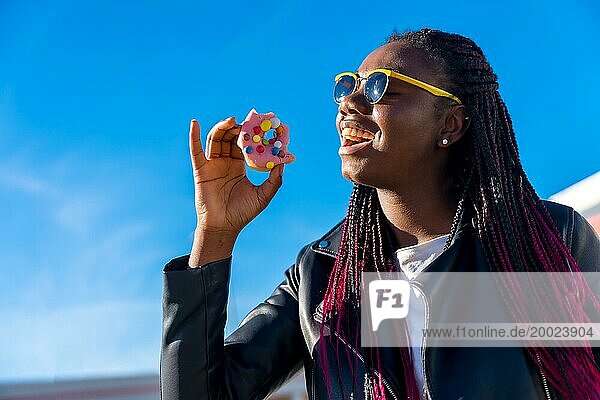 Glückliche afrikanische Frau  die an einem sonnigen Tag im Freien einen Donut isst