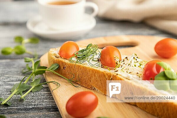 Langes Weißbrot Sandwich mit Frischkäse  Tomaten und Mikrogrün auf grauem Holzhintergrund und Leinenstoff. Seitenansicht  Nahaufnahme  selektiver Fokus