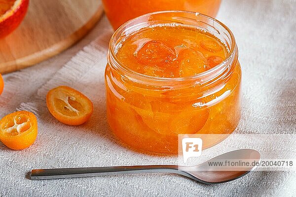 Orange and kumquat jam in a glass jar with fresh fruits on a white linen tablecloth. Homemade  close up