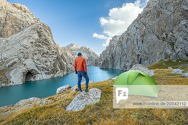 Young man with green tent at the turquoise mountain lake Kol Suu with rocky steep mountains  Kol Suu Lake  Sary Beles Mountains  Naryn Province  Kyrgyzstan  Asia