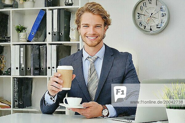 K generiert  Erfolgreicher Jungunternehmer sitzt zufrieden im Büro  30  35  Jahre  Mann  lächelt zufrieden  Existenzgründer  Firmenchef  trinkt einen Becher Kaffee