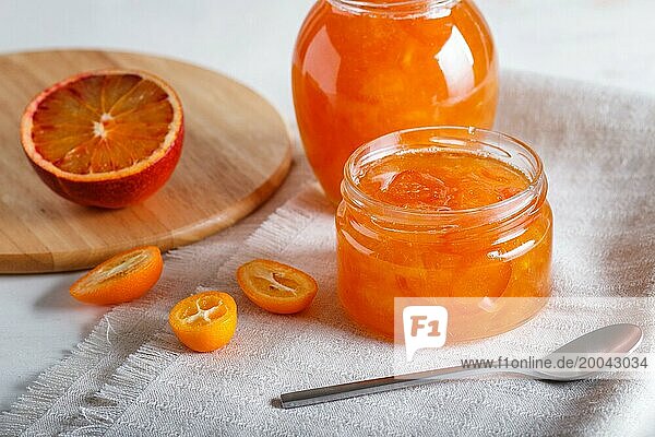 Orangen und Kumquatmarmelade in einem Glas mit frischen Früchten auf einer weißen Leinentischdecke. Hausgemacht  Nahaufnahme