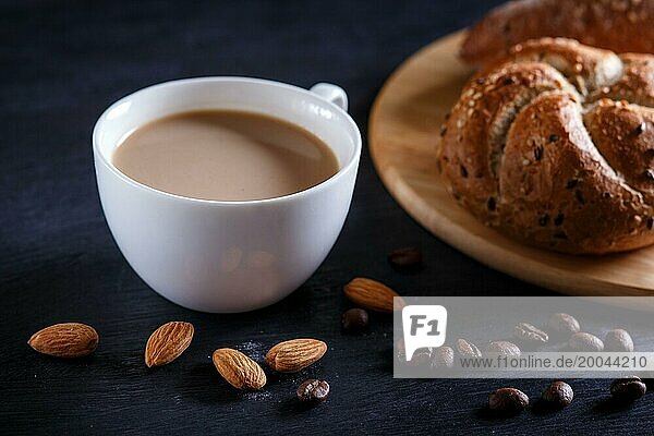 White cup of coffee with cream and buns on a black background. close up