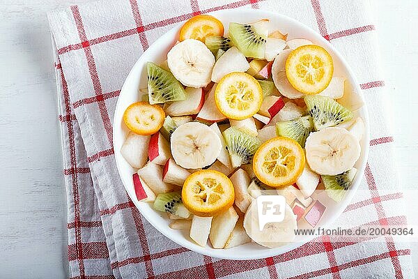 Vegetarischer Salat aus Bananen  Äpfeln  Birnen  Kumquats und Kiwi auf Leinentischdecke  Draufsicht  flat lay  weißer Holzhintergrund