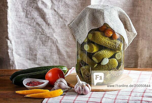 Pickled cucumbers and tomatoes in a glass jar on linen tablecloth and wooden table. Homemade  copy space