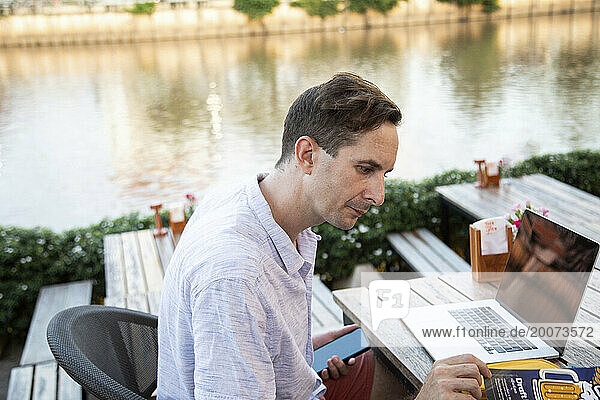 Young man stops to check the menu  he's working on his laptop in a riverside restaurant