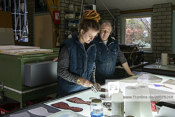 Apprentice female stained glass worker being taught lessons from teacher. Leanring over lightbox colouring in glass