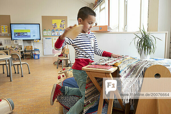Young boy practising ironing at pre school table  doing house work
